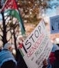 A rally advocating for Palestinian rights, featuring a prominent protest sign and Palestinian flag in the background.