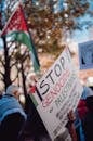 A rally advocating for Palestinian rights, featuring a prominent protest sign and Palestinian flag in the background.